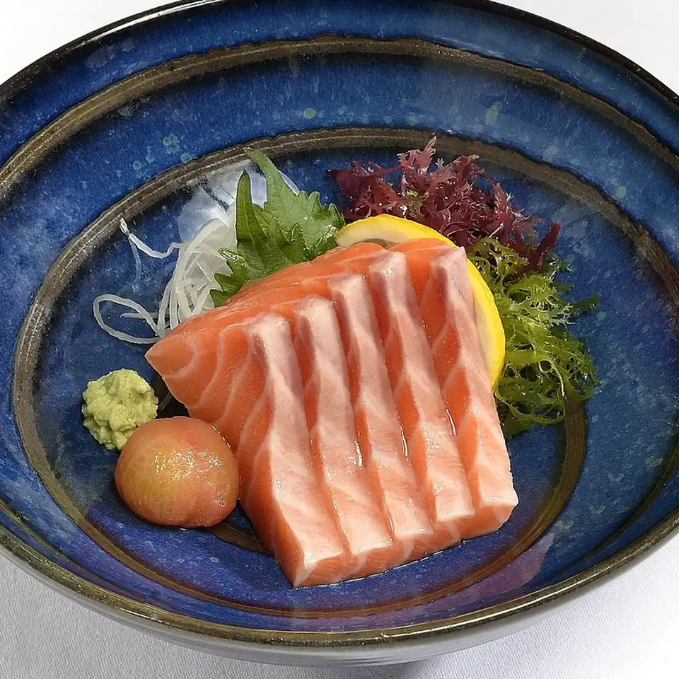 Slices of ocean trout with wasabi and citrus in a deep blue ceramic bowl