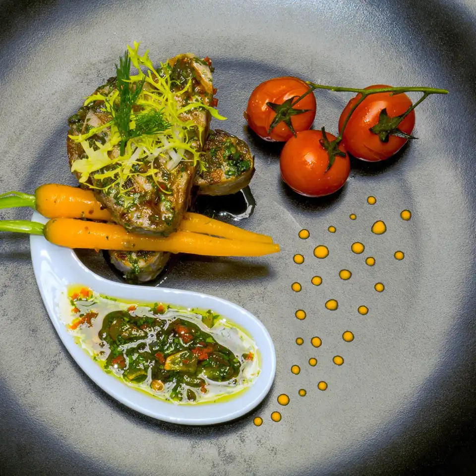A grey plate of charred baby carrots, heirloom tomatoes and green sambal in a porcelain spoon