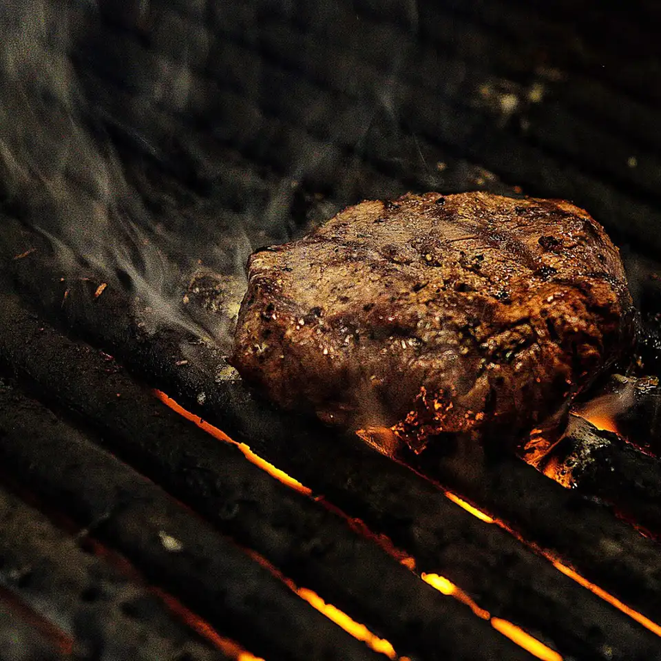 Dry-aged striploin searing over glowing binchotan coals, smoke rising