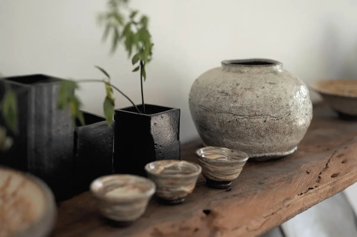 House ceramics — a stone jar and thrown cups on a timber bench